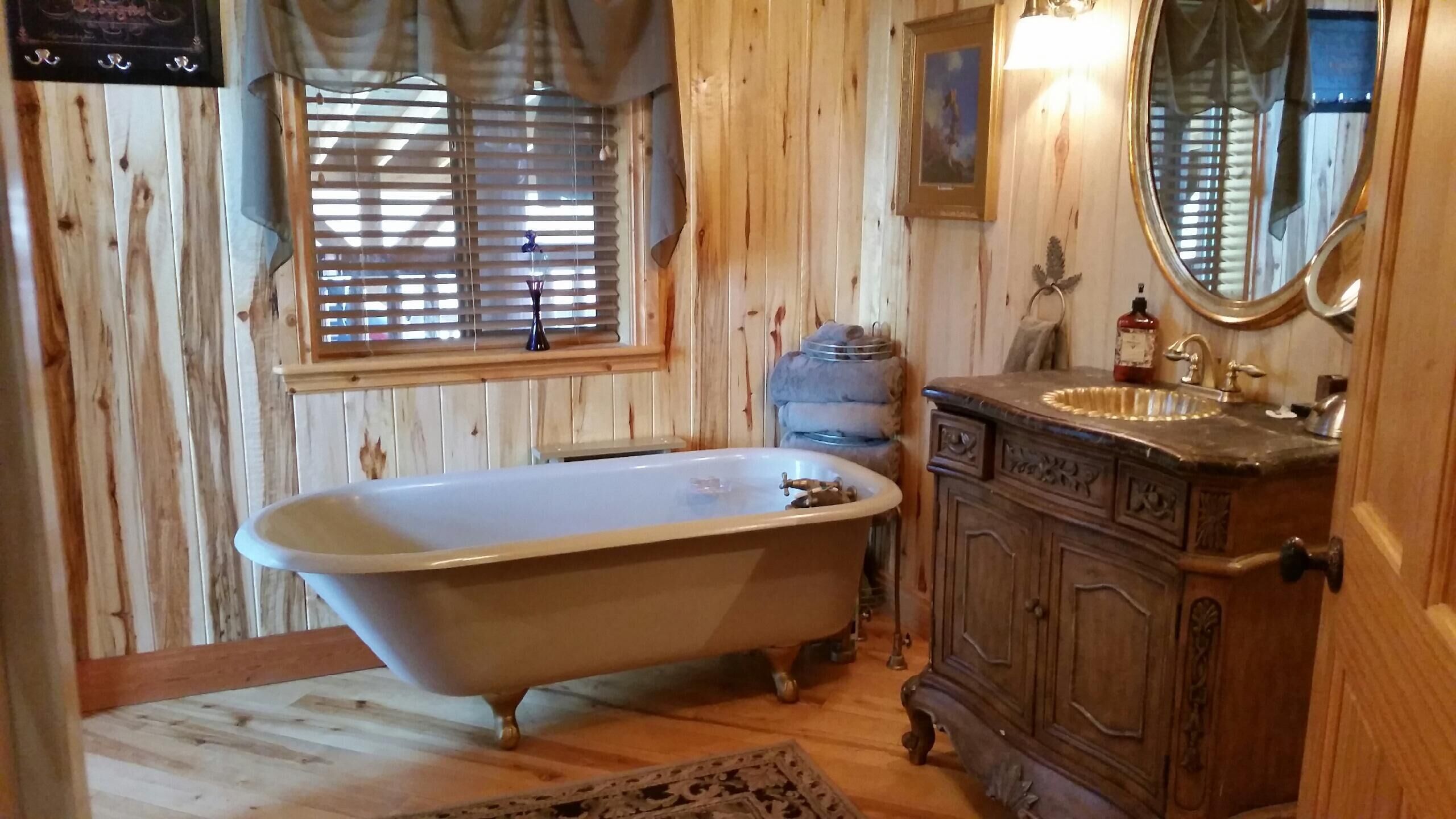 A wooden-paneled bathroom with a clawfoot bathtub, a sink with a mirror, and a window with blinds.