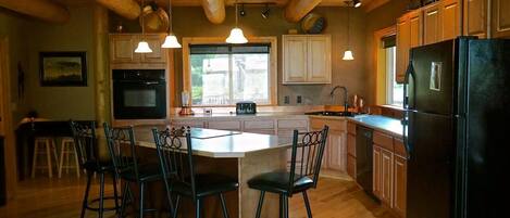 A kitchen with wooden beams, a central island with chairs, and a refrigerator.