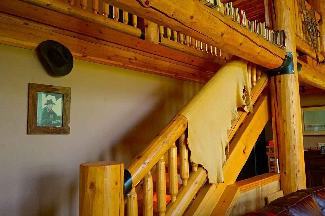 Un escalier en bois avec une main courante recouverte d’un tissu déchiré, un tableau encadré accroché au mur et un chapeau suspendu au mur.