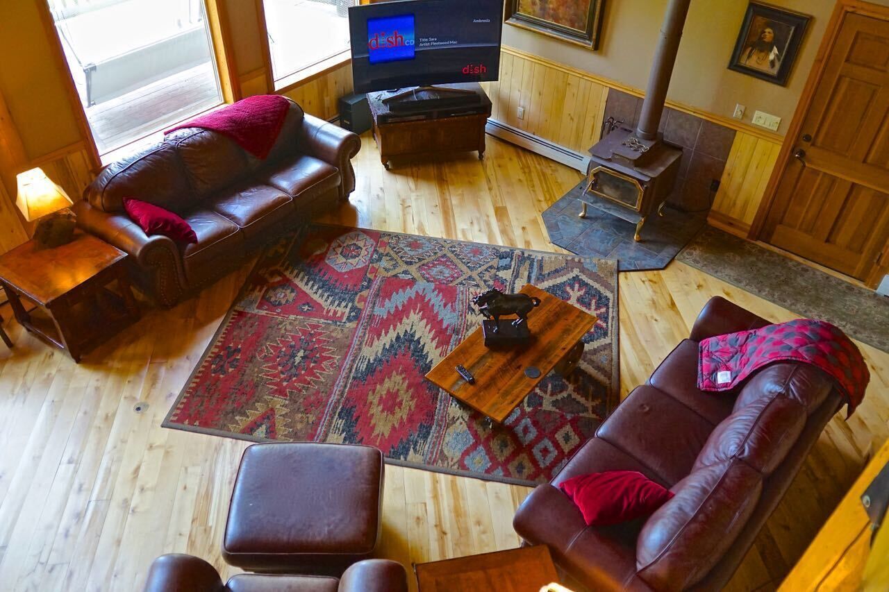 Una sala de estar acogedora con un sofá de cuero, un tapete estampado, una mesa de centro, una televisión y una chimenea.
