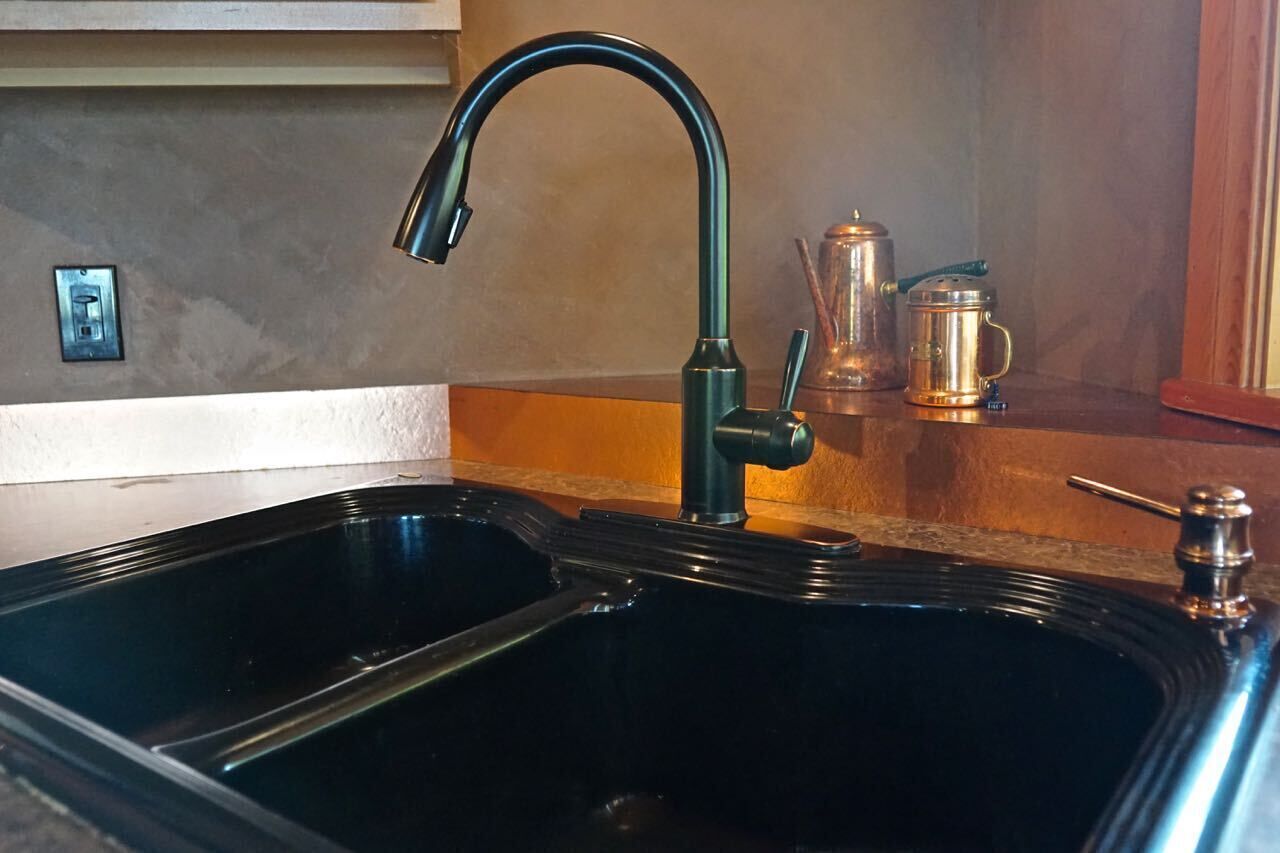 A kitchen with a black sink, a green faucet, and a coffee pot on the counter.