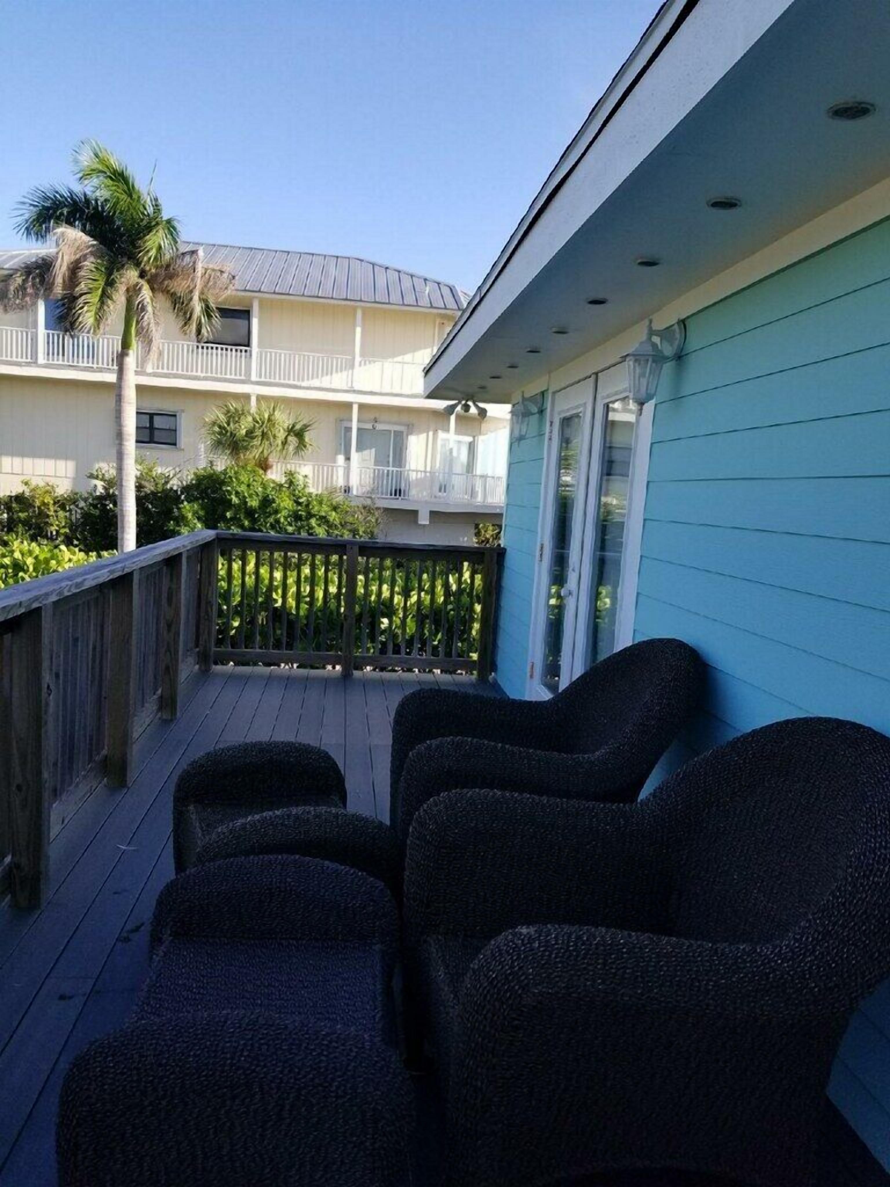 A balcony with wicker furniture, a wooden railing, and a view of a building with balconies and palm trees.
