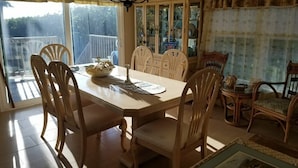 Un comedor con una mesa lista para cuatro personas, rodeada de sillas de madera. Se ve un aparador con puertas de vidrio al fondo.