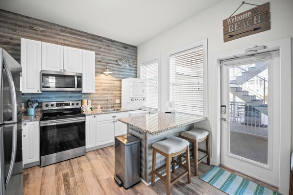 Una cocina moderna con armarios blancos, electrodomésticos de acero inoxidable y una pared decorada con madera.