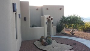 Un bâtiment de style désertique, avec des murs recouverts d’enduit, un portail en métal et des cactus dans l’aménagement paysager.