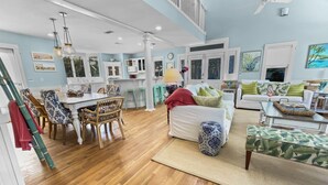 A spacious living room with a dining area, white furniture, and a staircase leading to an upper level. - "Breakers" | 2 Minutes walk to the Beach | Heated community pool | Includes 4 Bikes (Seaside)