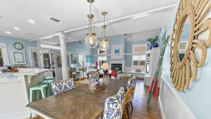 A spacious dining area with a wooden table and patterned chairs, a kitchen with white cabinetry, and a living area with a fireplace. - "Breakers" | 2 Minutes walk to the Beach | Heated community pool | Includes 4 Bikes (Seaside)