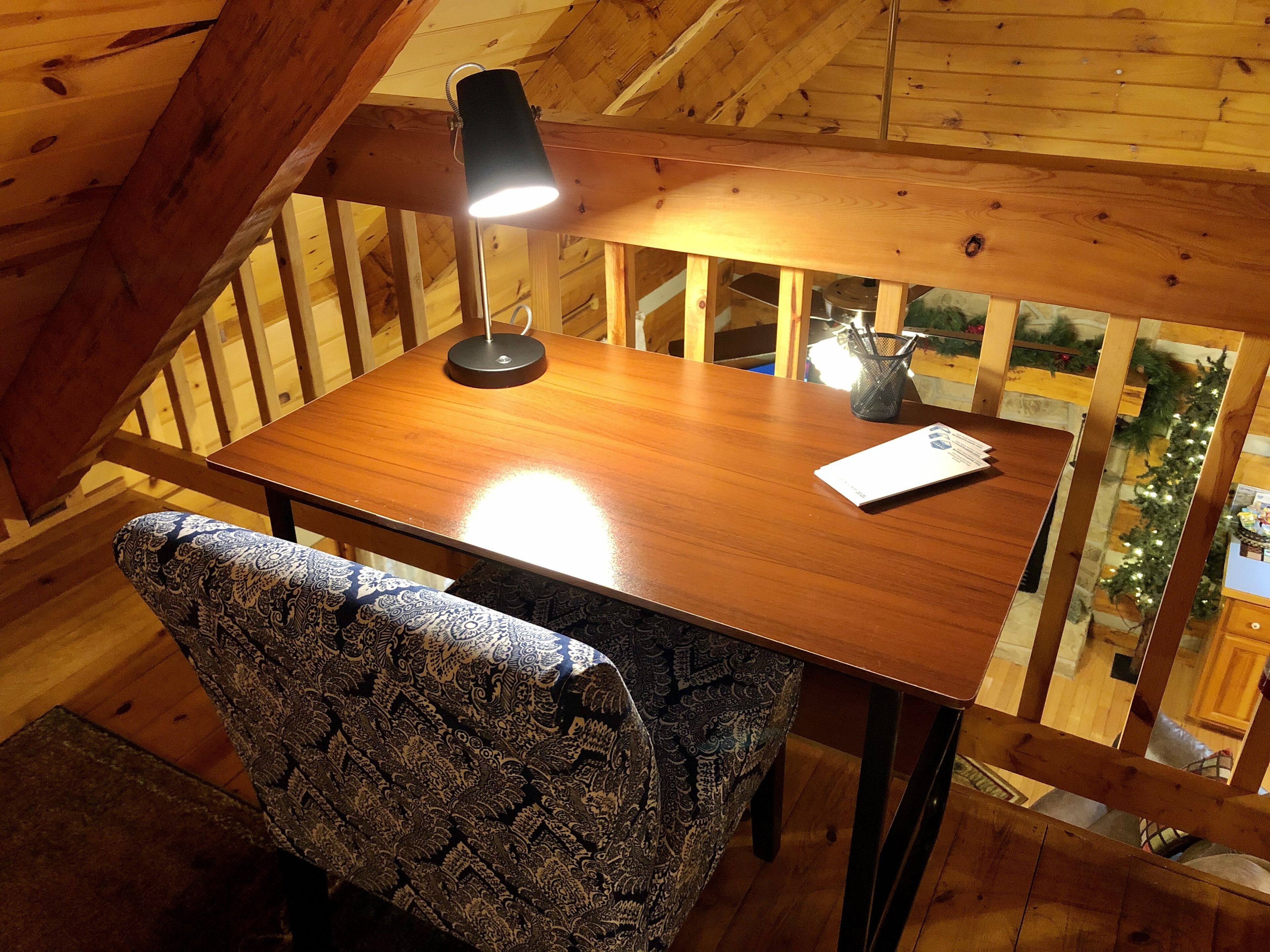 Una mesa de madera para comer con una lámpara, una silla con diseño y vistas a zonas verdes afuera.