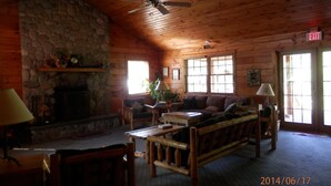Interior de una cabaña de troncos con chimenea de piedra, muebles de madera y un ventilador de techo.