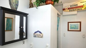 A bathroom with a mirror, a sign reading "Aloha," and a "Gone Surfing" sign above the shower.