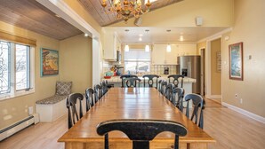 A spacious dining area with a long wooden table and chairs, a chandelier, and a view of the kitchen in the background. - Spacious Santa Cruz Beach Home, Walk to the Ocean, Game Room, Pet Friendly! (Santa Cruz)