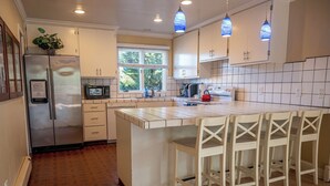 A kitchen with white cabinets, a stainless steel refrigerator, a microwave, a kettle, and a large island with bar stools. - Spacious Santa Cruz Beach Home, Walk to the Ocean, Game Room, Pet Friendly! (Santa Cruz)
