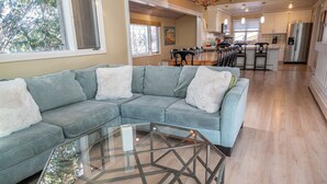 A living room with a sectional sofa, a glass coffee table, and a kitchen in the background. - Spacious Santa Cruz Beach Home, Walk to the Ocean, Game Room, Pet Friendly! (Santa Cruz)