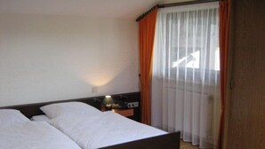 Quarto de hotel com uma cama grande, mesa de cabeceira com abajur e guarda-roupa de madeira.