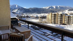 A balcony with wooden chairs and a view of a snowy mountain and buildings.