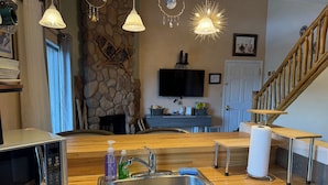 A kitchen with a stainless steel sink, a microwave, and a stone wall.