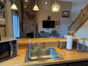A kitchen with a stainless steel sink, a microwave, and a stone wall.