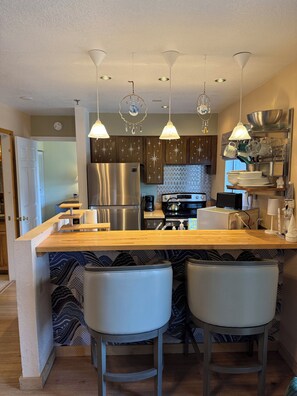 A modern kitchen with a central island, pendant lights, stainless steel appliances, and patterned wallpaper. - Come Experience SkiTopia-True Ski In/Out Condo Steps from the SilverQueen Lift (Crested Butte)