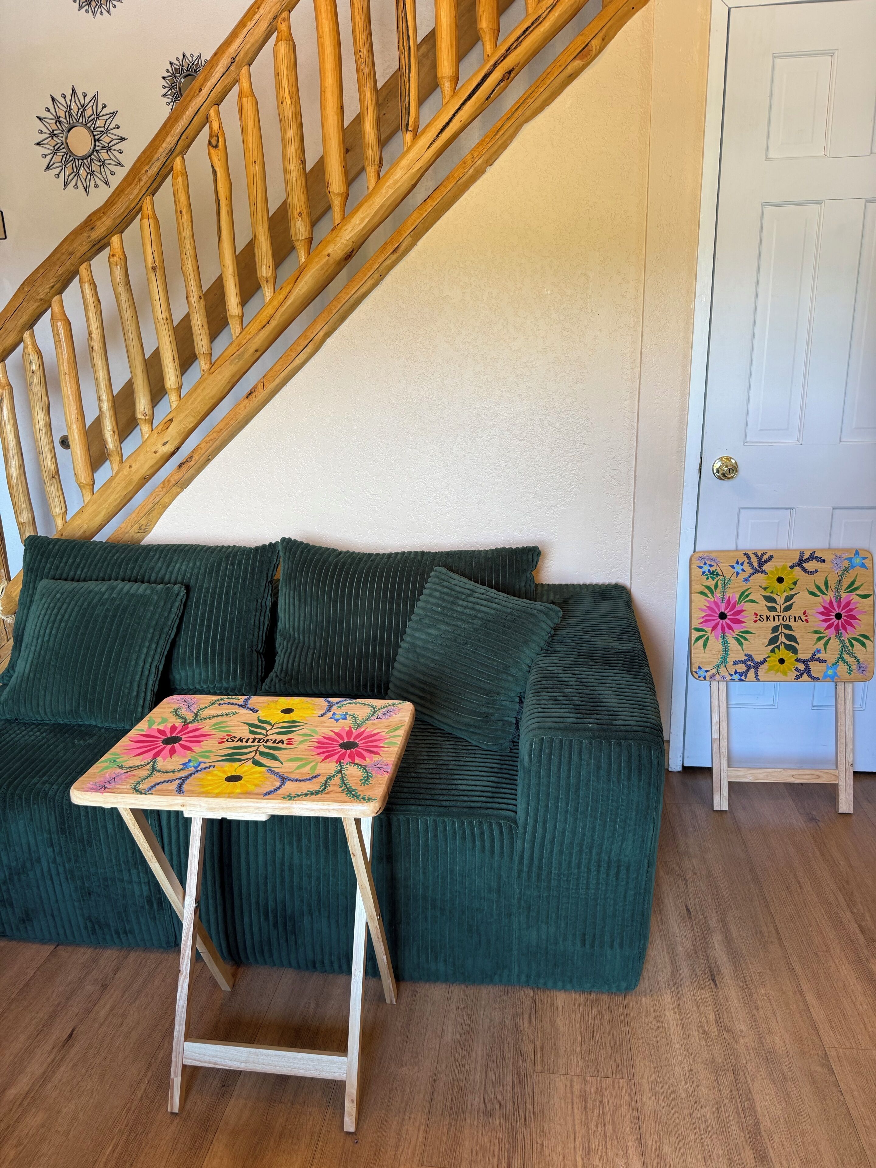 A green sofa with a small wooden table in front, a wooden staircase, and a white door.