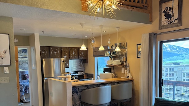 A modern kitchen with a central island, bar stools, and a dining area.