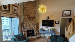 A living room with a stone fireplace, a television, and a staircase.