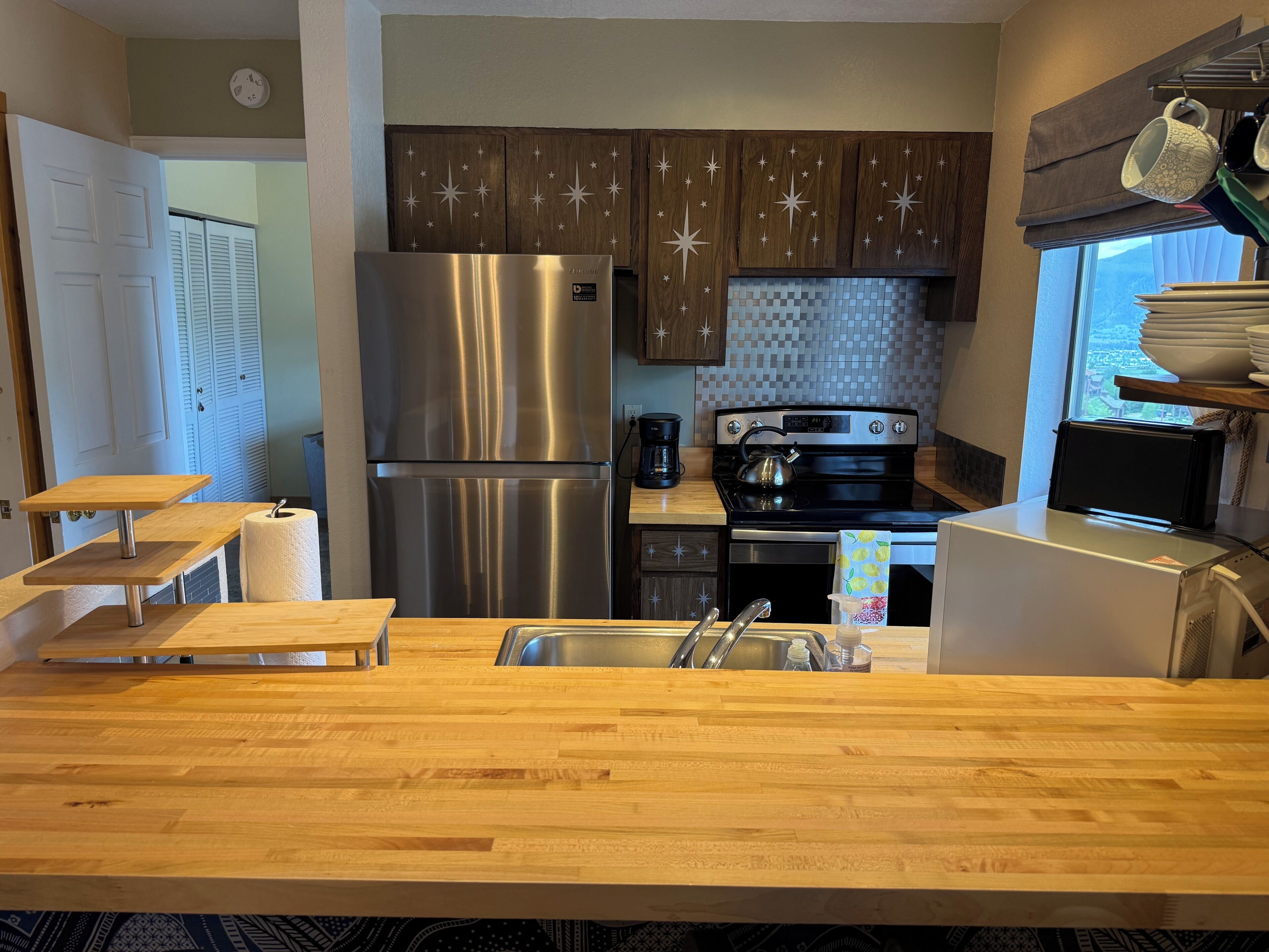 A modern kitchen with a stainless steel refrigerator, a built-in oven, a sink, and wooden countertops.