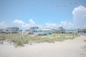A beachfront property with multiple houses, a sandy path, and a clear sky. - Moon Struck: Oceanfront Home with Bold, Coastal Flair (Oak Island)