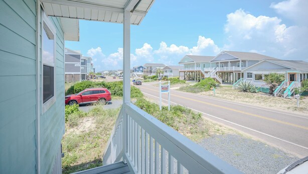 A coastal view from a porch with a road, houses, and a signboard. - Moon Struck: Oceanfront Home with Bold, Coastal Flair (Oak Island)