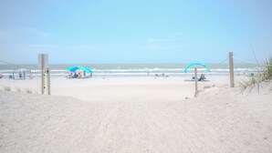 Una playa con un sendero de arena que lleva al agua, sombrillas y sillas.
