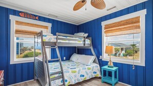A bunk bed room with a view of a house through the window. - Moon Struck: Oceanfront Home with Bold, Coastal Flair (Oak Island)