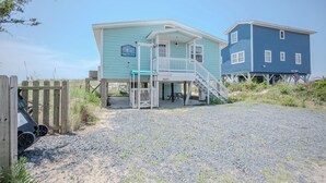 A beachfront property with a covered porch, a staircase leading to a deck, and a two-story building. - Moon Struck: Oceanfront Home with Bold, Coastal Flair (Oak Island)