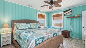 Un dormitorio con cama, mesitas de noche, lámpara, ventilador de techo y ventana con vistas.