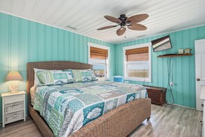 Un dormitorio con cama, mesitas de noche, lámpara, ventilador de techo y ventana con vistas.