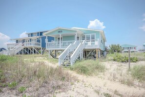 A beachfront house with a covered porch, multiple decks, and a staircase leading to the entrance.