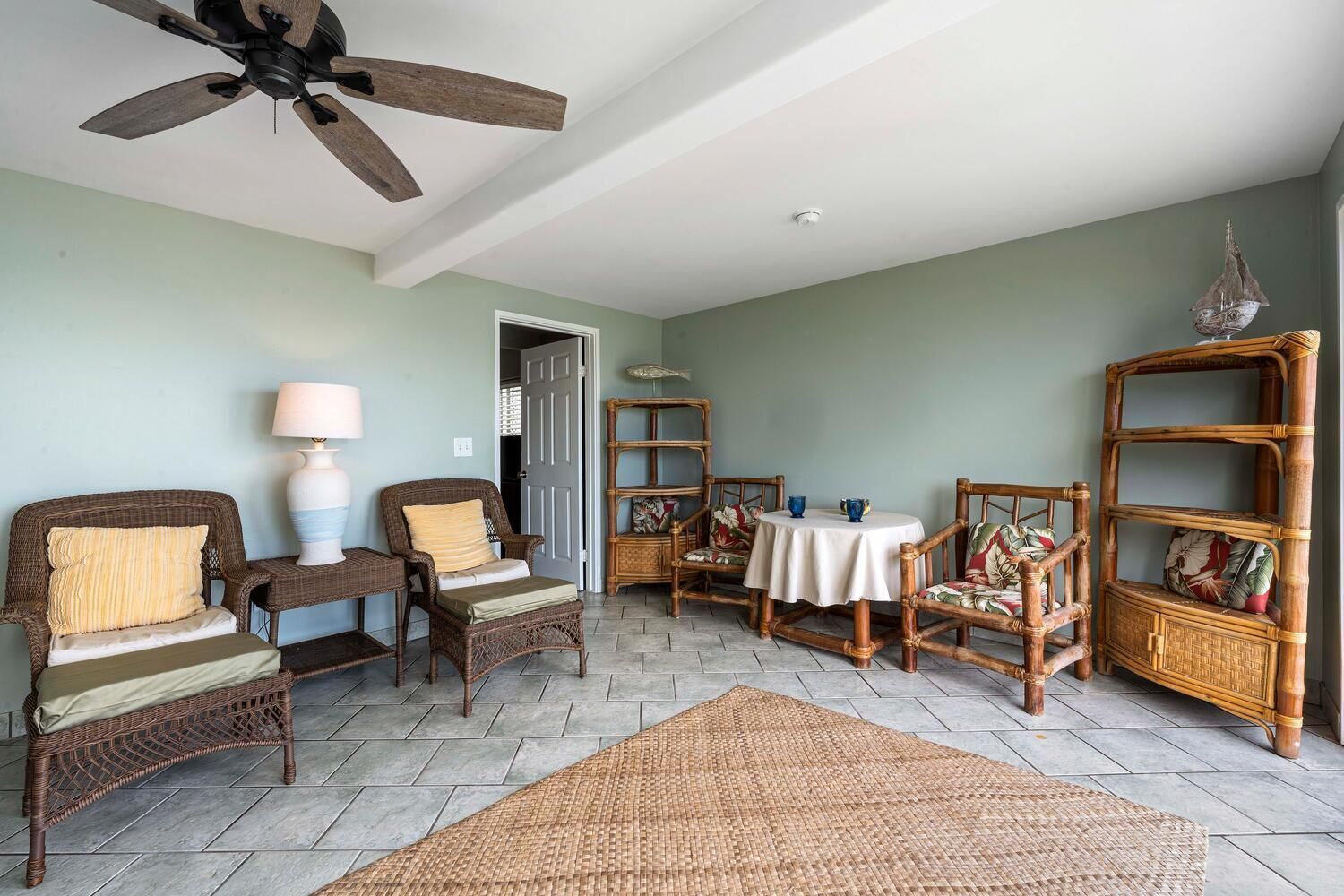 Una habitación con mobiliario de mimbre, un ventilador de techo y una mesa con mantel blanco.