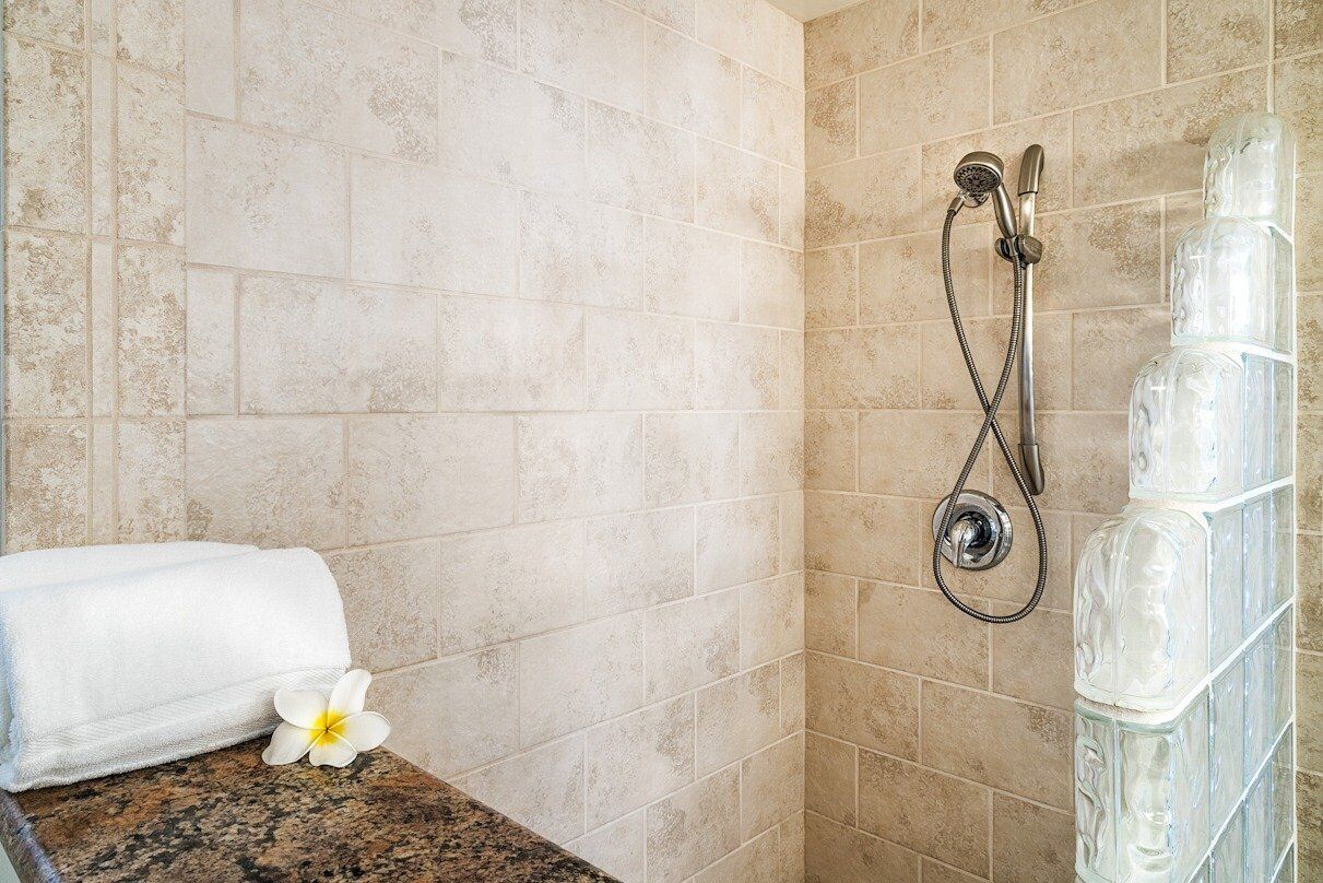 A bathroom with beige tiles, a shower with a glass enclosure, a white towel, and a white flower.