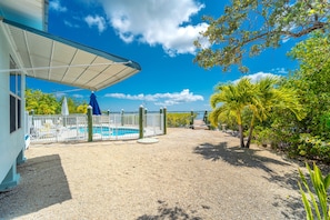 Ein Poolbereich mit überdachter Terrasse, umzäuntem Schwimmbecken und umliegender Bepflanzung.