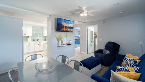 A modern living room with a glass dining table, a blue sofa, and a ceiling fan.