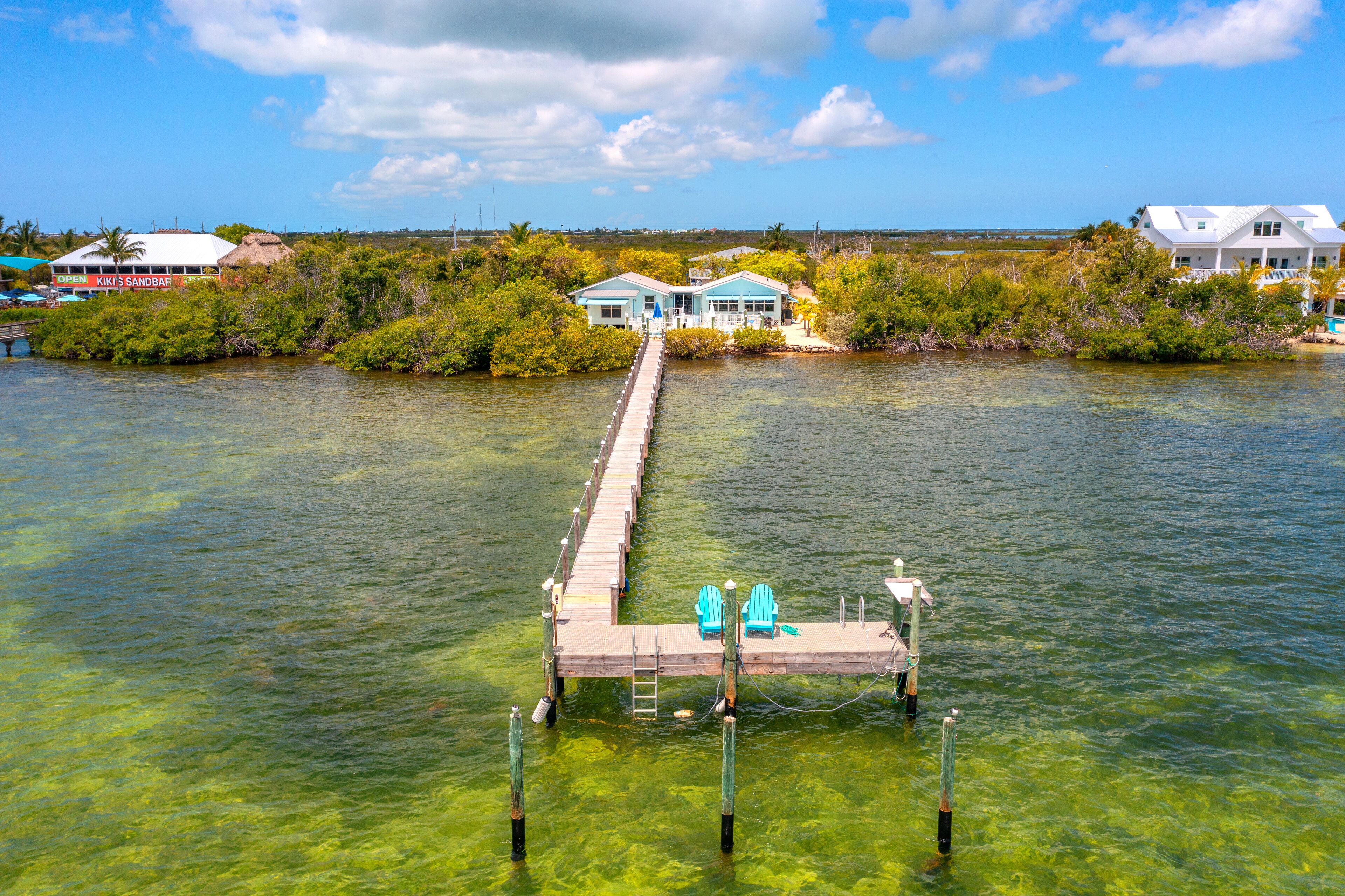 A dock extending into clear water with two blue chairs at the end.