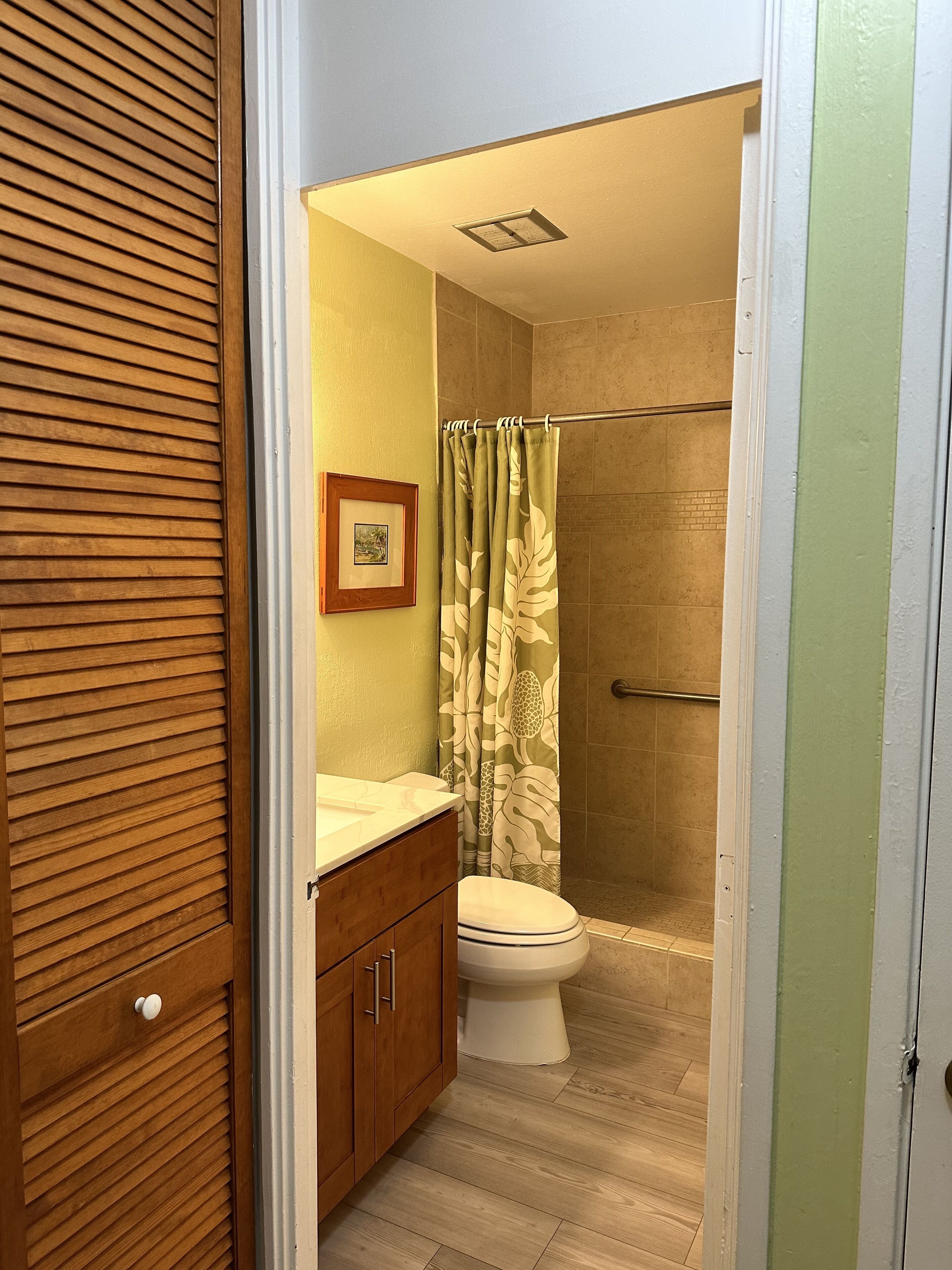 A bathroom with a wooden vanity, a toilet, a shower with a glass door, and a framed picture on the wall.