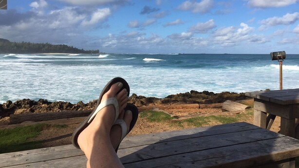 Eine hölzerne Bank mit Blick auf einen Strand, Wellen und einen klaren Himmel.