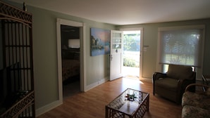 A room with a wooden floor, a glass coffee table, a chair, a door leading to a balcony, and a painting on the wall.