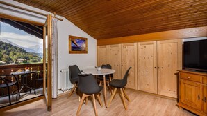 Ett mysigt rum med ett träpanelat tak, ett matbord med stolar, ett element och en tv som står på ett träskåp.