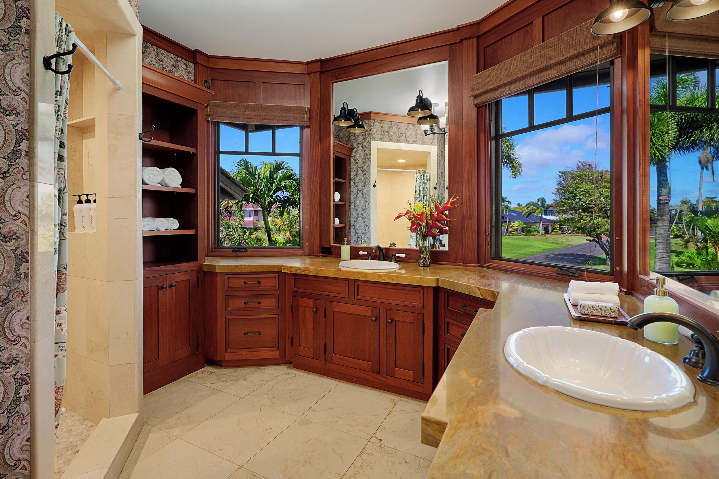 A spacious bathroom with a large sink, wooden cabinets, and a view of a tropical landscape.