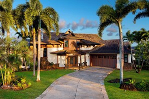 A two-story house with a stone facade, a tiled roof, and a driveway leading to a garage. - Hale Lani - Custom Built Ocean view Home on Golf Course with A/C (Koloa)