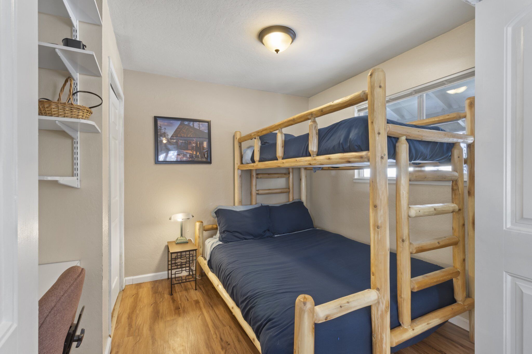 Een slaapkamer met een stapelbed, een houten ladder, een klein tafeltje met een lamp en een lijst met een afbeelding aan de muur.