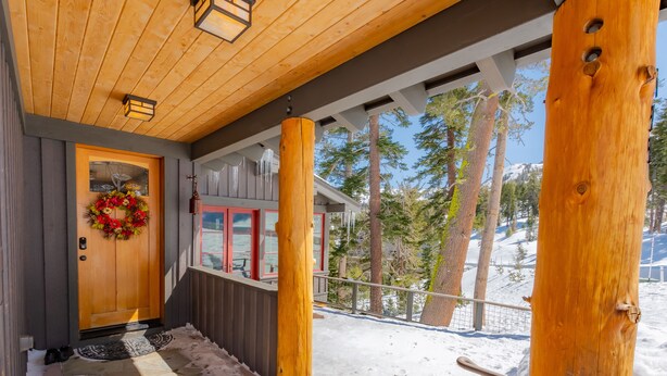 A wooden porch with a red door, a wreath, and a view of snow-covered trees. - Perle du Bois - Ski in/Ski out (Kirkwood)