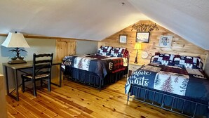 A cozy attic bedroom with two beds, wooden flooring, a desk, and a lamp.