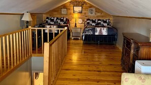 A loft bedroom with two beds, wooden flooring, a staircase, and a wooden dresser.