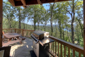A wooden deck with a grill and picnic table overlooking a forested area.